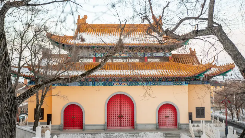 Traditional Chinese temple building behind winter branches, with red doors and orange roof tiles.