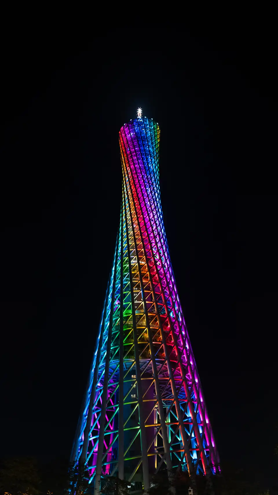 Tower-like structure at night with colorful lights against a dark background.