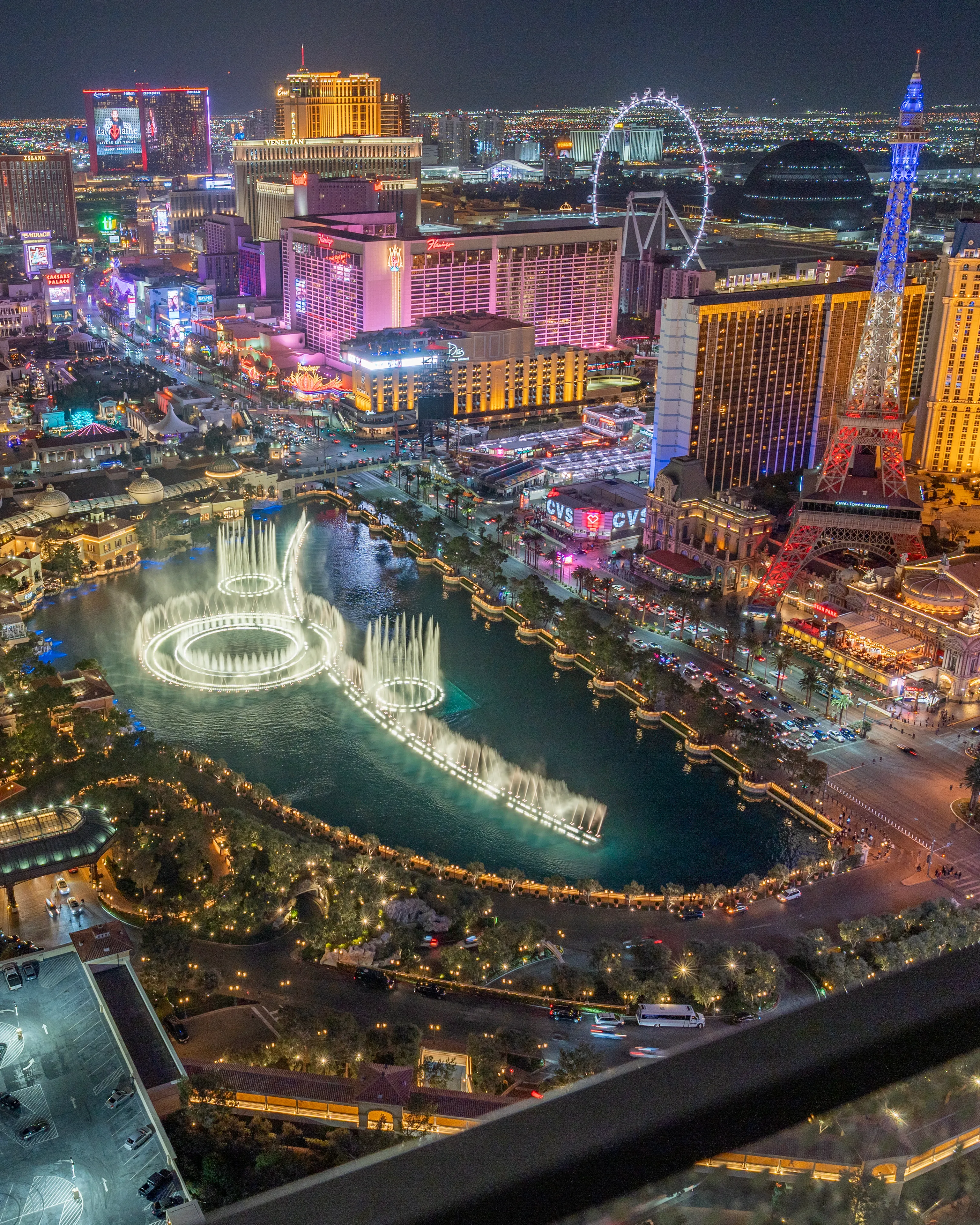 Night view of the Las Vegas Strip with neon lights, a Ferris wheel, and city buildings from above.