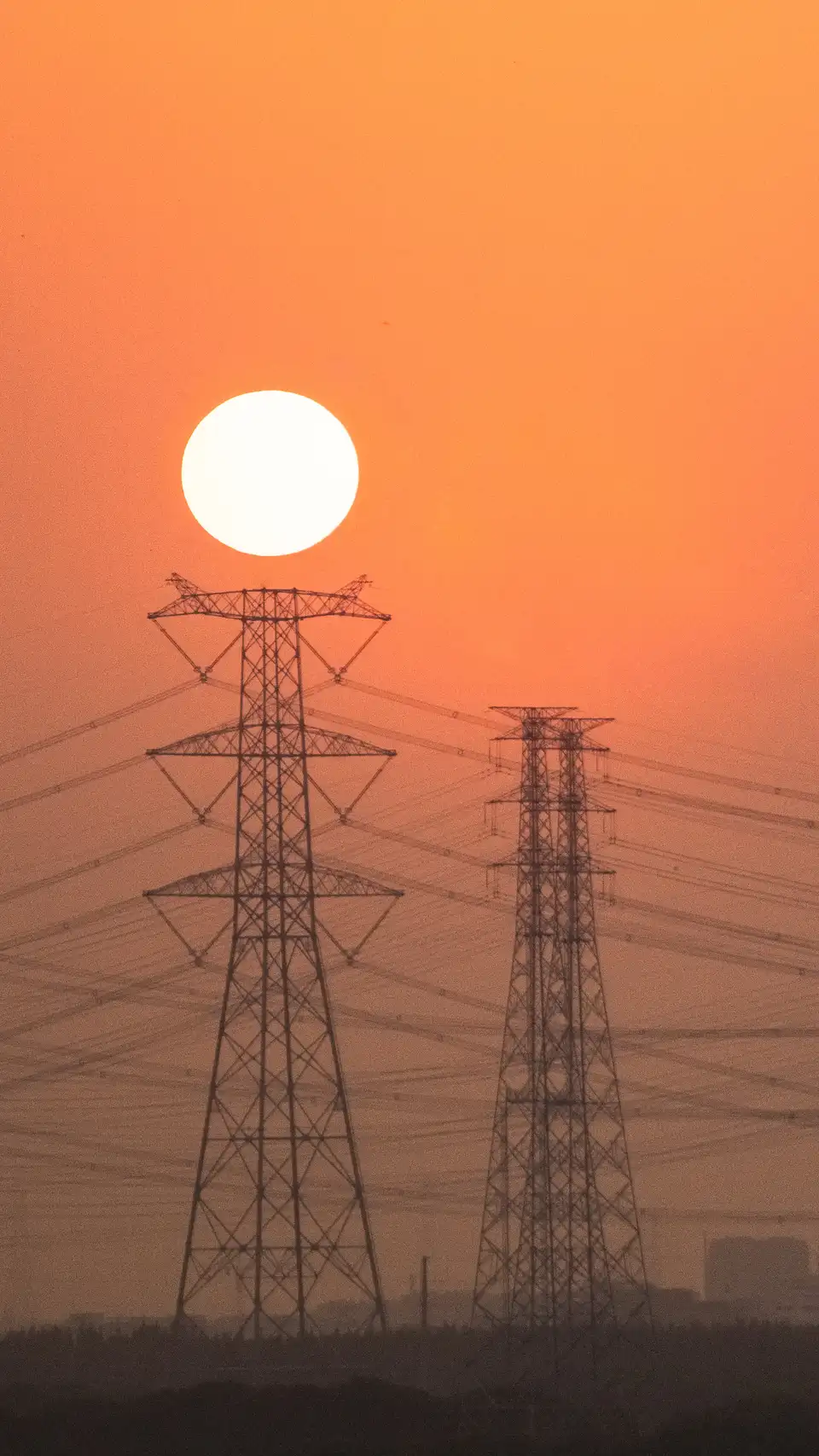 Power towers and lines in Shanghai at sunset, with an orange sun near the city edge.